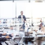 -Corporate meeting in a glass-walled office with professionals working on laptops