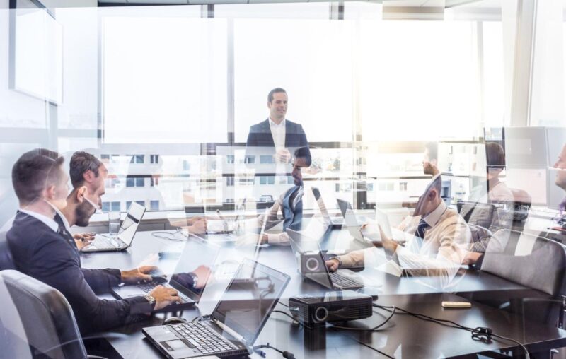 -Corporate meeting in a glass-walled office with professionals working on laptops